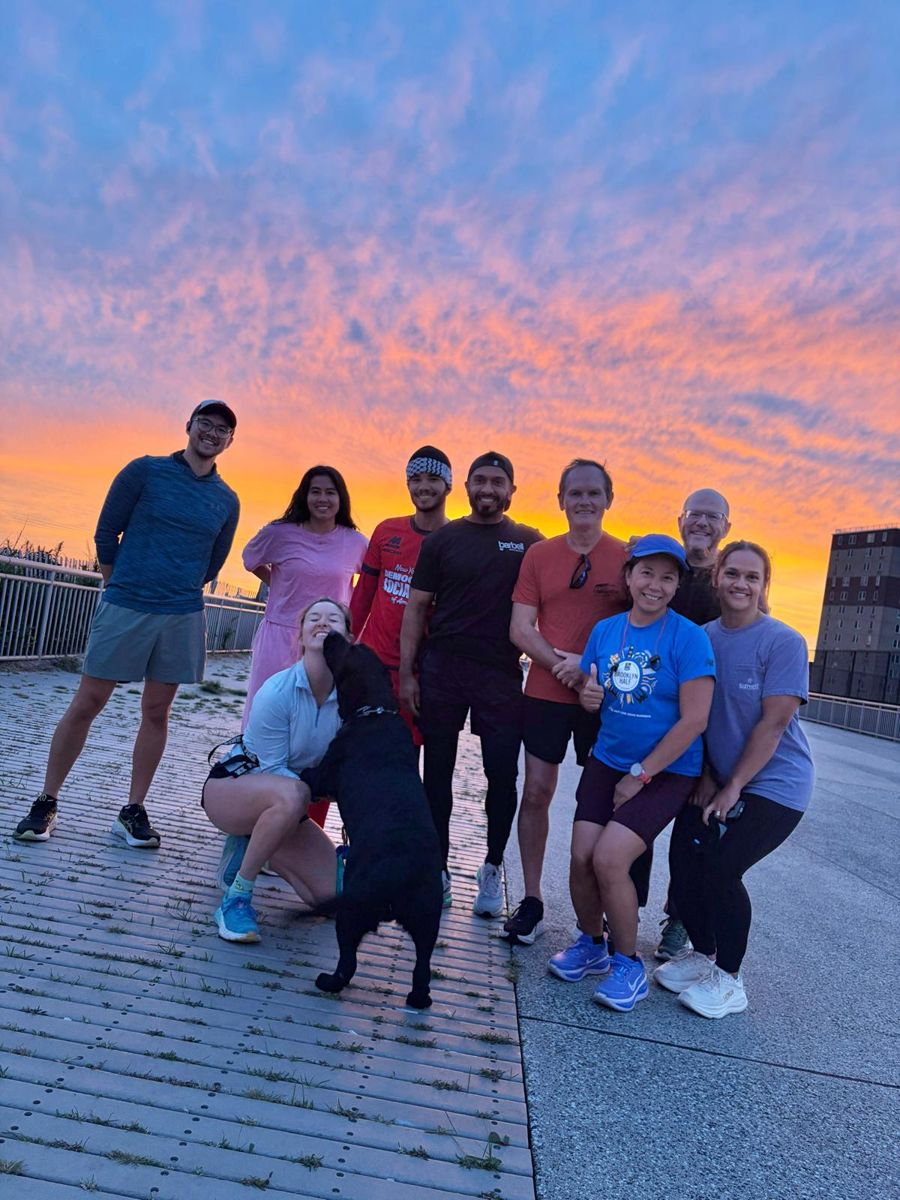 Rockaway Run Club members and a dog posing on the boardwalk under an orange sunset