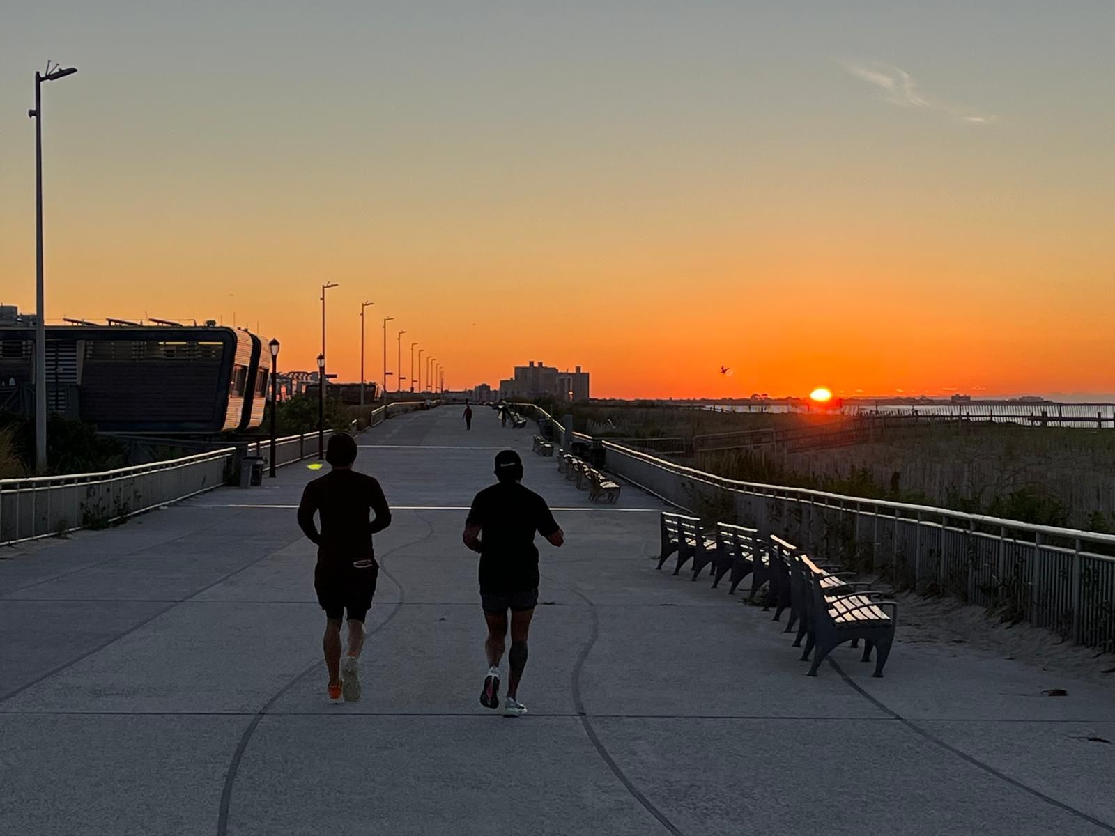 Two runners on the Rockaway boardwalk at sunrise, the sun just over the ocean